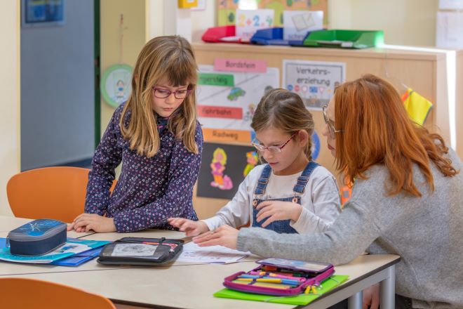 Zwei Kindern sitzen zusammen mit einer Schulassistenz an einem Tisch und basteln.